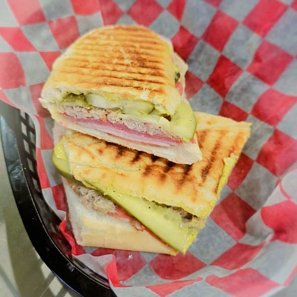 A Cuban sandwich from Poppy's Smokehouse, cut in half, with pickles, ham, and pork.