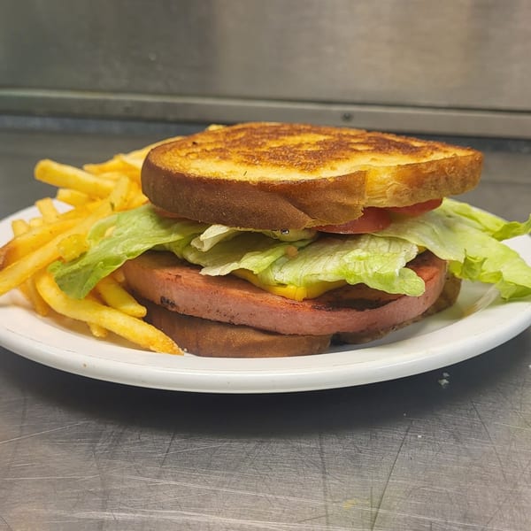 A Poppy's Smokehouse bologna sandwich with lettuce, tomato, and cheese, served with fries.