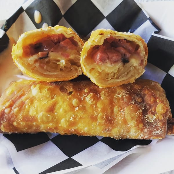 A golden-brown egg roll, cut in half to reveal a savory filling of meat and cheese, on checkered paper.