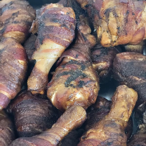 Close-up of several bacon-wrapped chicken drumsticks, some with charred skin, from Poppy's Smokehouse.