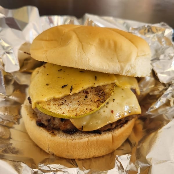 Poppy's Smokehouse burger with melted cheese and sliced pears, wrapped in foil.